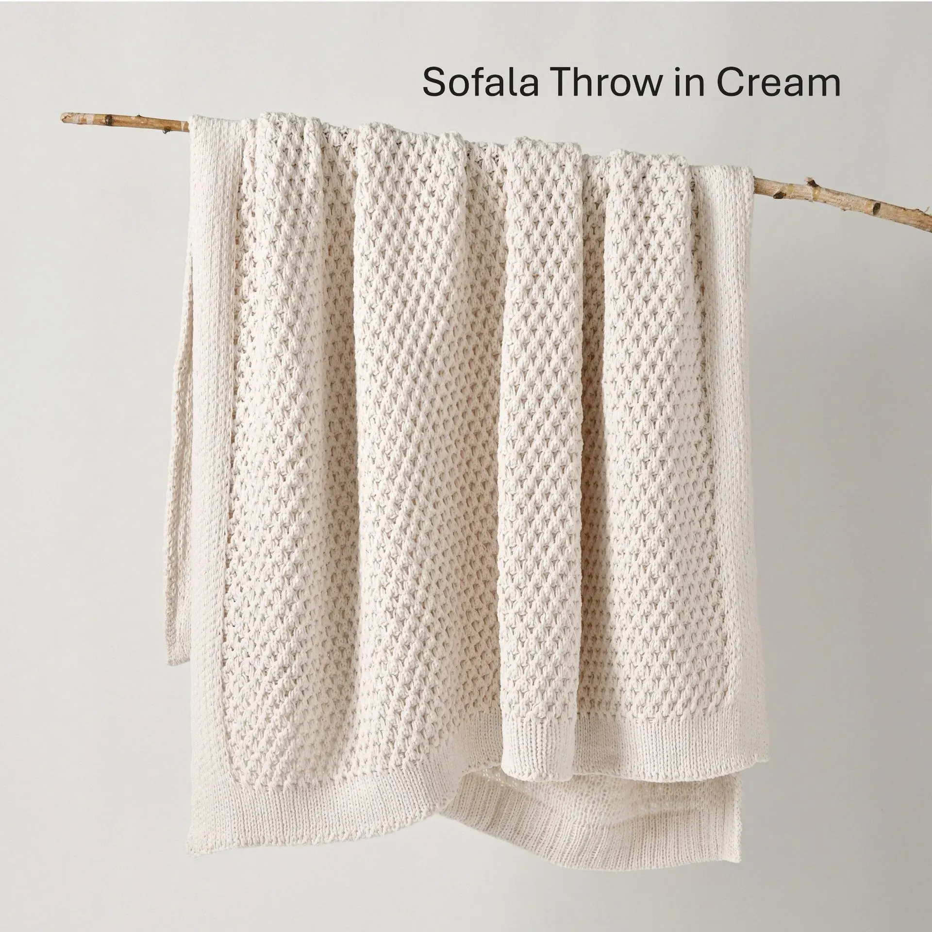 Cream knit throw blanket draped over a wooden rod on a light wall