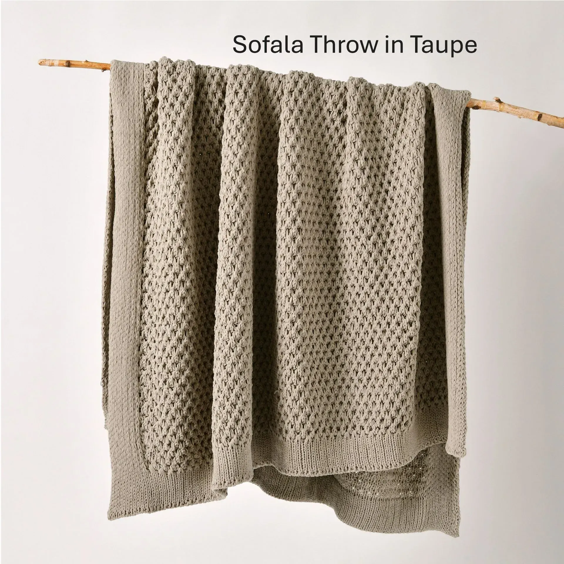 Taupe knitted throw blanket draped over a wooden rod against a light background