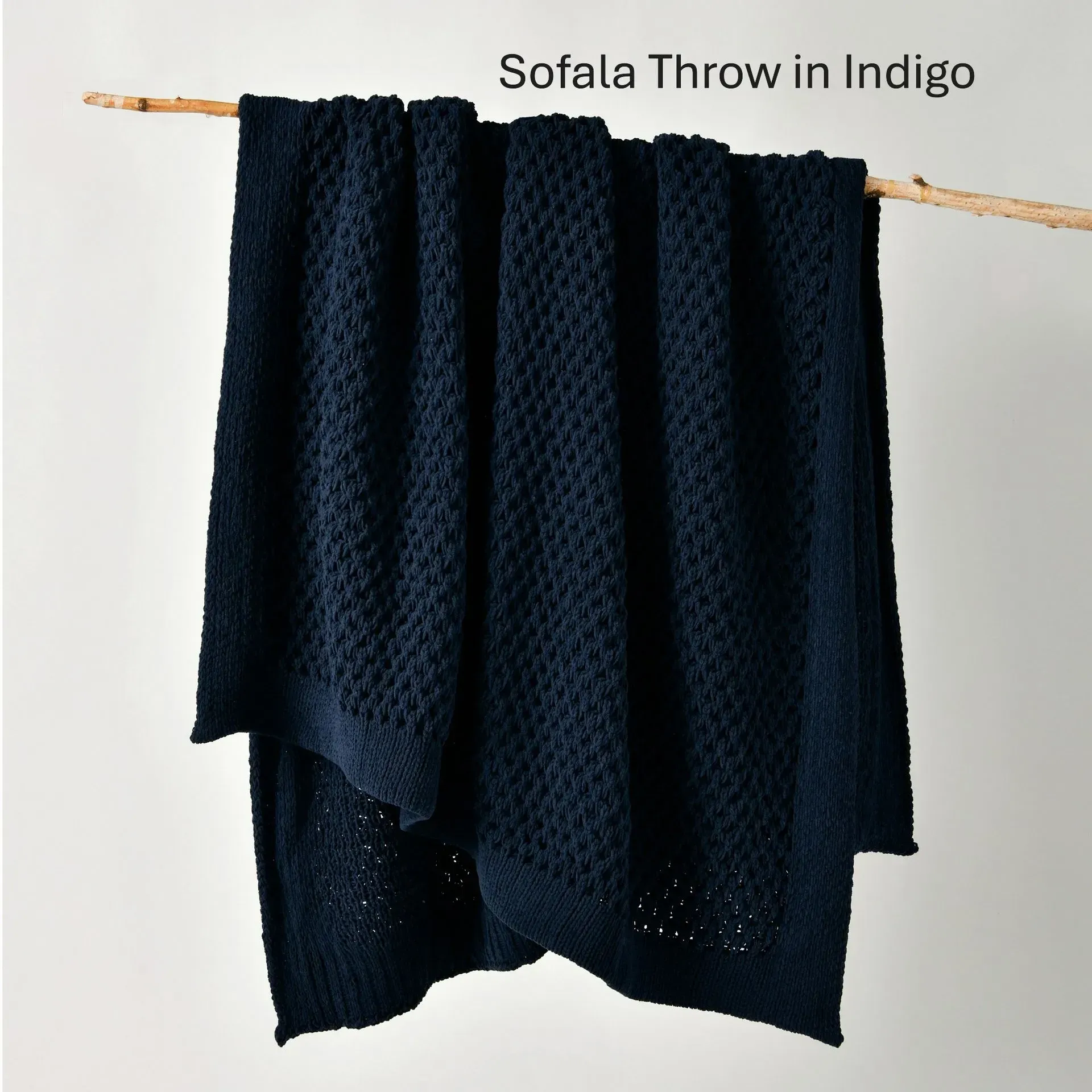 Dark indigo throw blanket draped over a wooden rod against a light wall