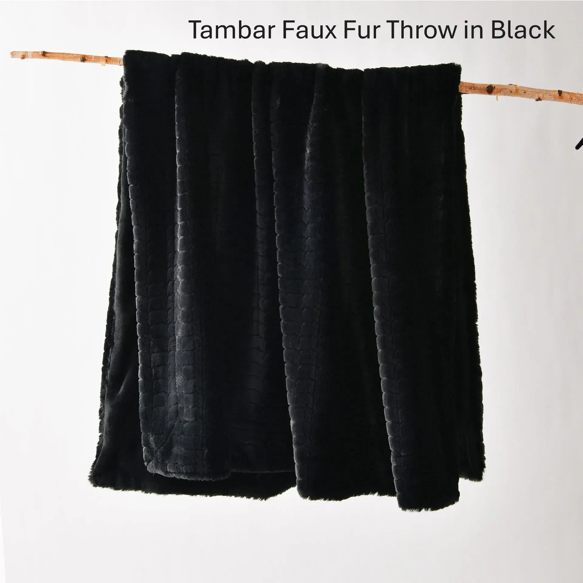 Black faux fur throw draped over a wooden rod against a white background