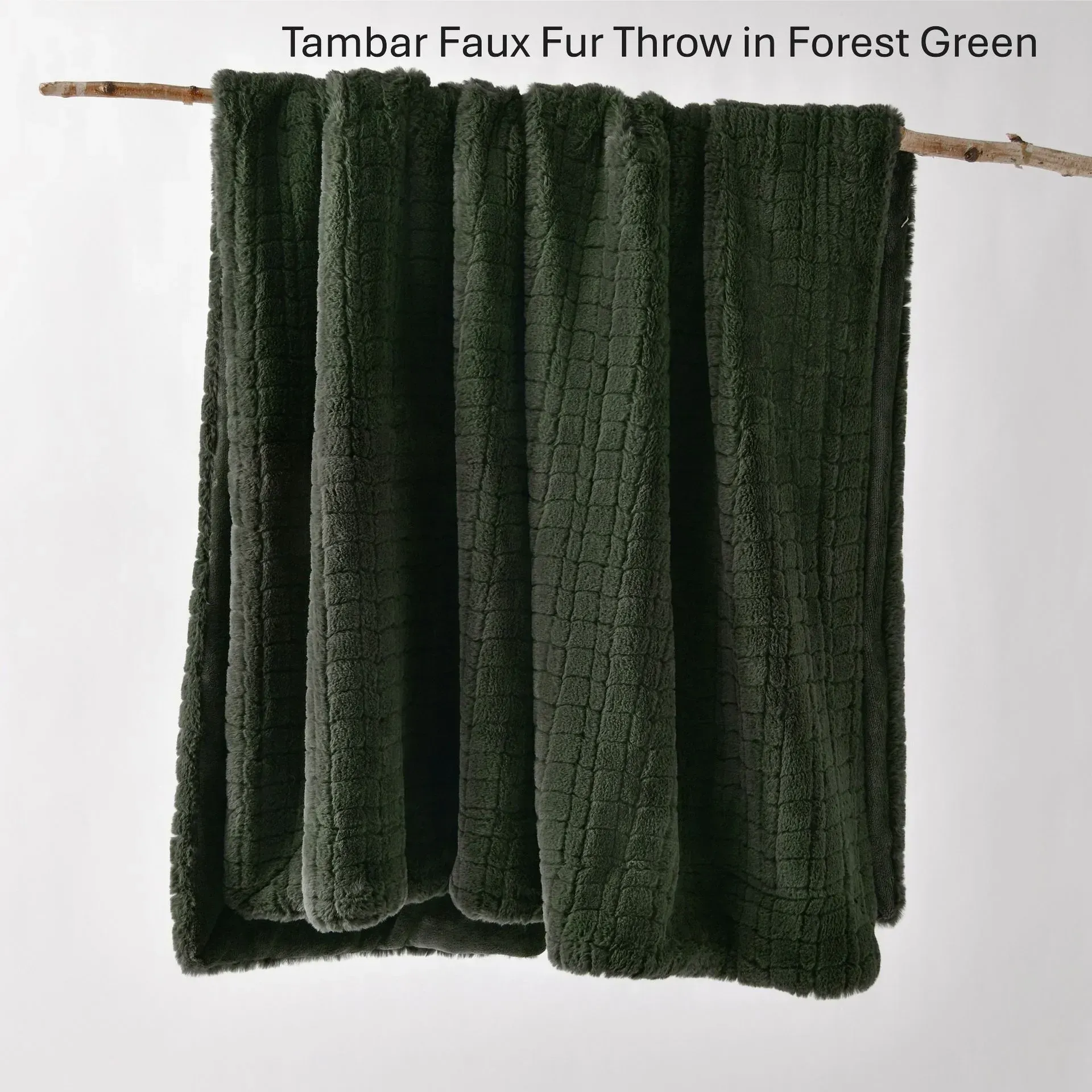 Dark forest green faux fur throw blanket draped over a branch, with the text “Tambar Faux Fur Throw in Forest Green”