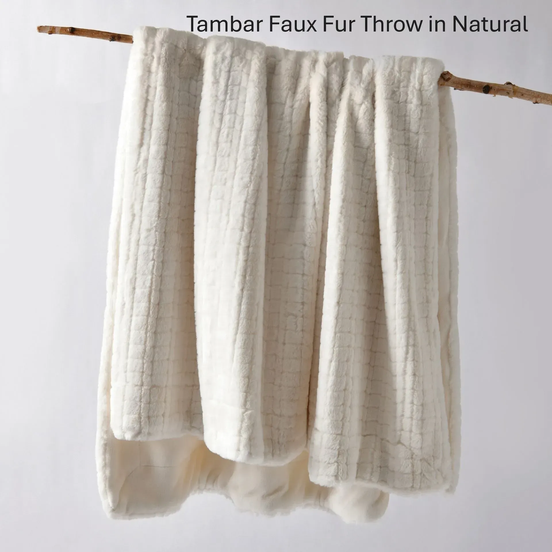 Cream faux fur throw draped over a natural wooden rod against a light background
