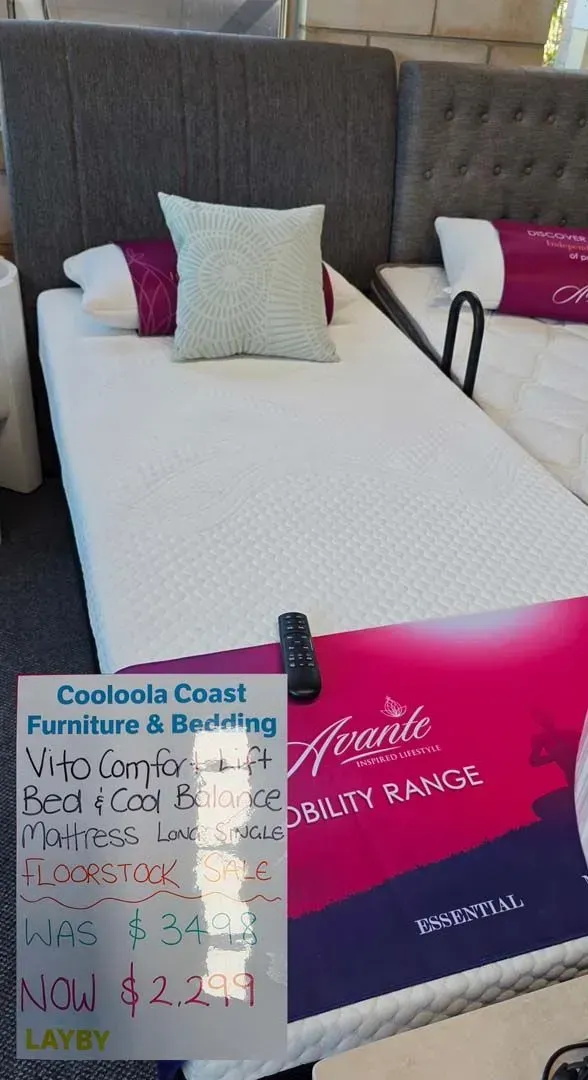 Store display of a white adjustable bed with a blue-and-pink “CoolaCoast Furniture & Bedding” sign.