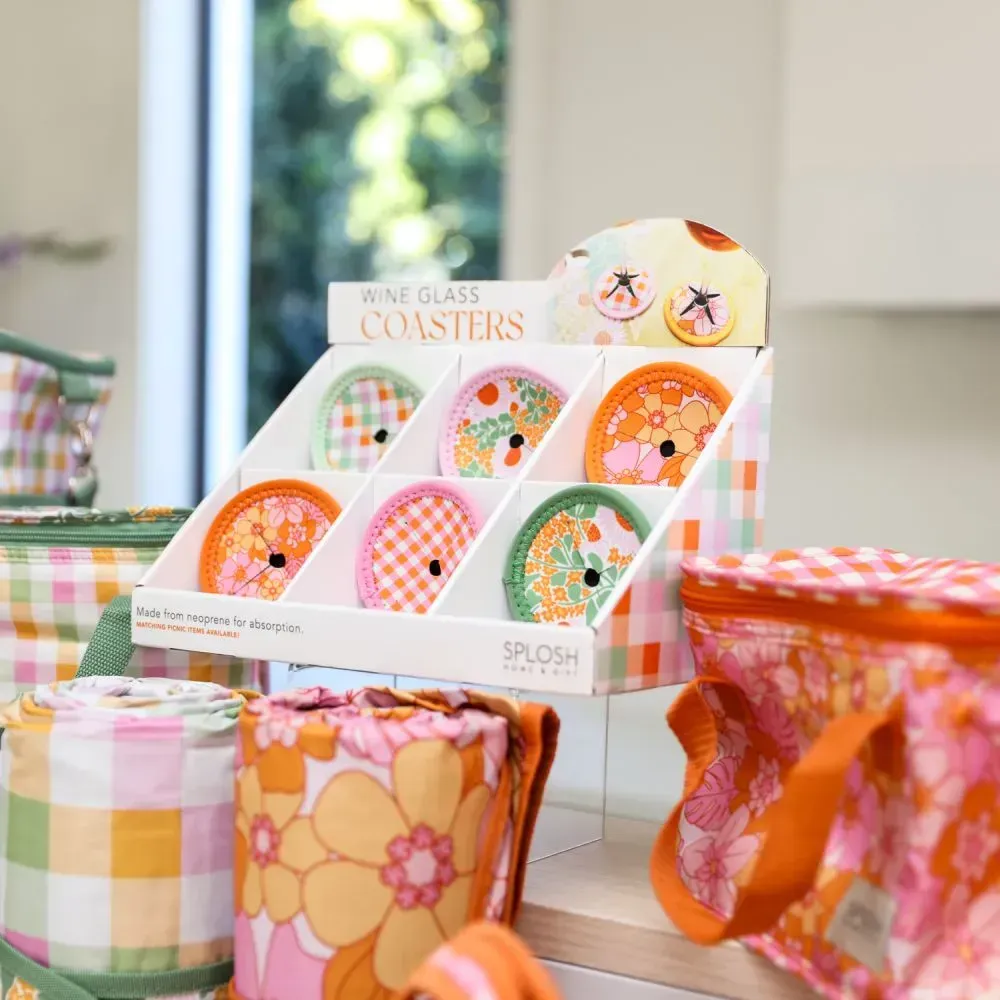 Assorted colorful glass coasters in a display box on a table, with floral-patterned fabric items nearby