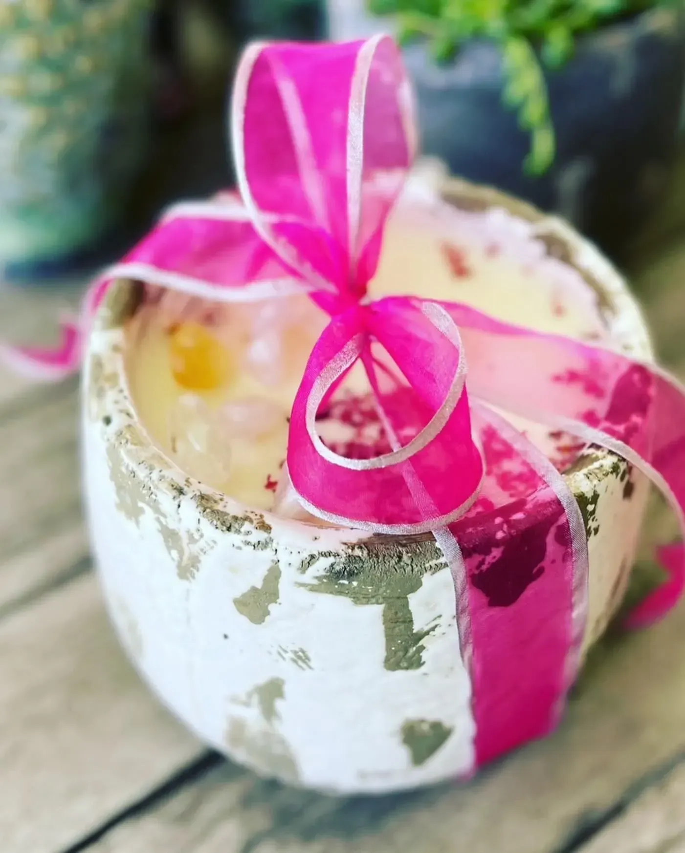 Pink ribbon tied around a small white gift box with gold accents on a wooden surface.