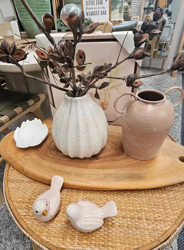 Ceramic vases and small bird figurines arranged on a round wooden tray in a shop display