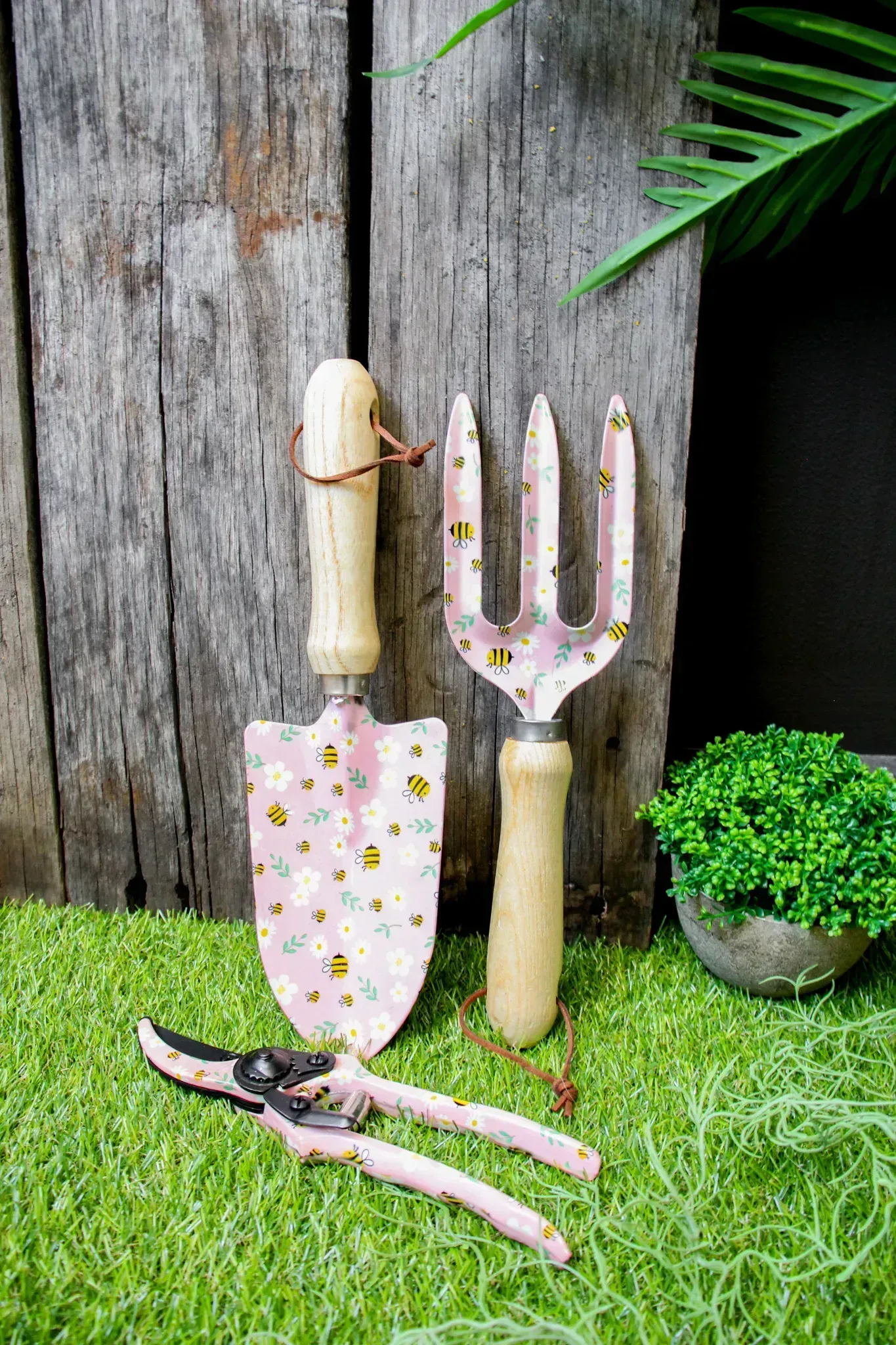 Garden scarecrow figures by a rustic wooden fence, with a pink polka-dot dress and pitchfork in grass.