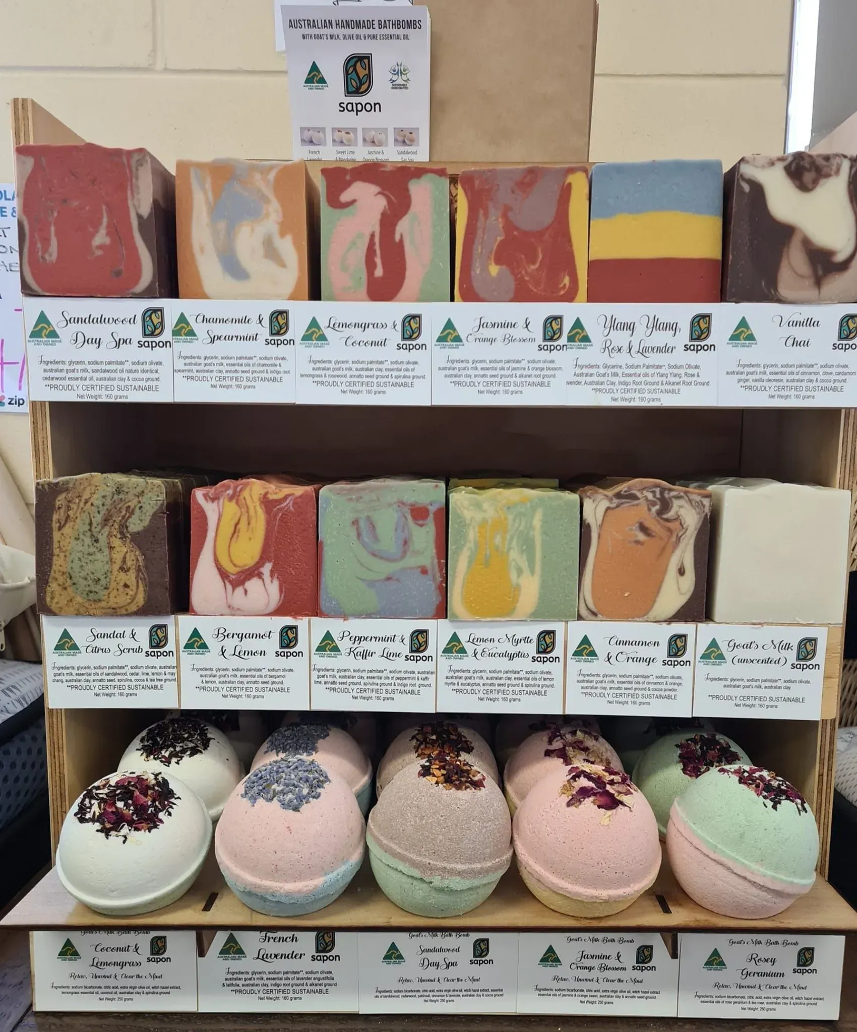 Display of colorful handmade soaps on shelves, each with a label and decorative toppings