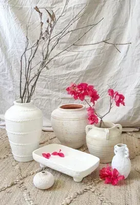 White ceramic vases with bare branches and pink flowers on a rustic white backdrop