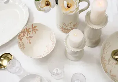 Elegant white table setting with floral plates, candles, and gold accents