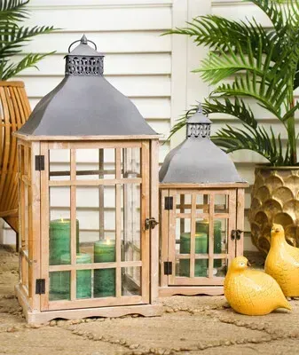 Two rustic lanterns with candles beside yellow pears and green plants on a stone patio