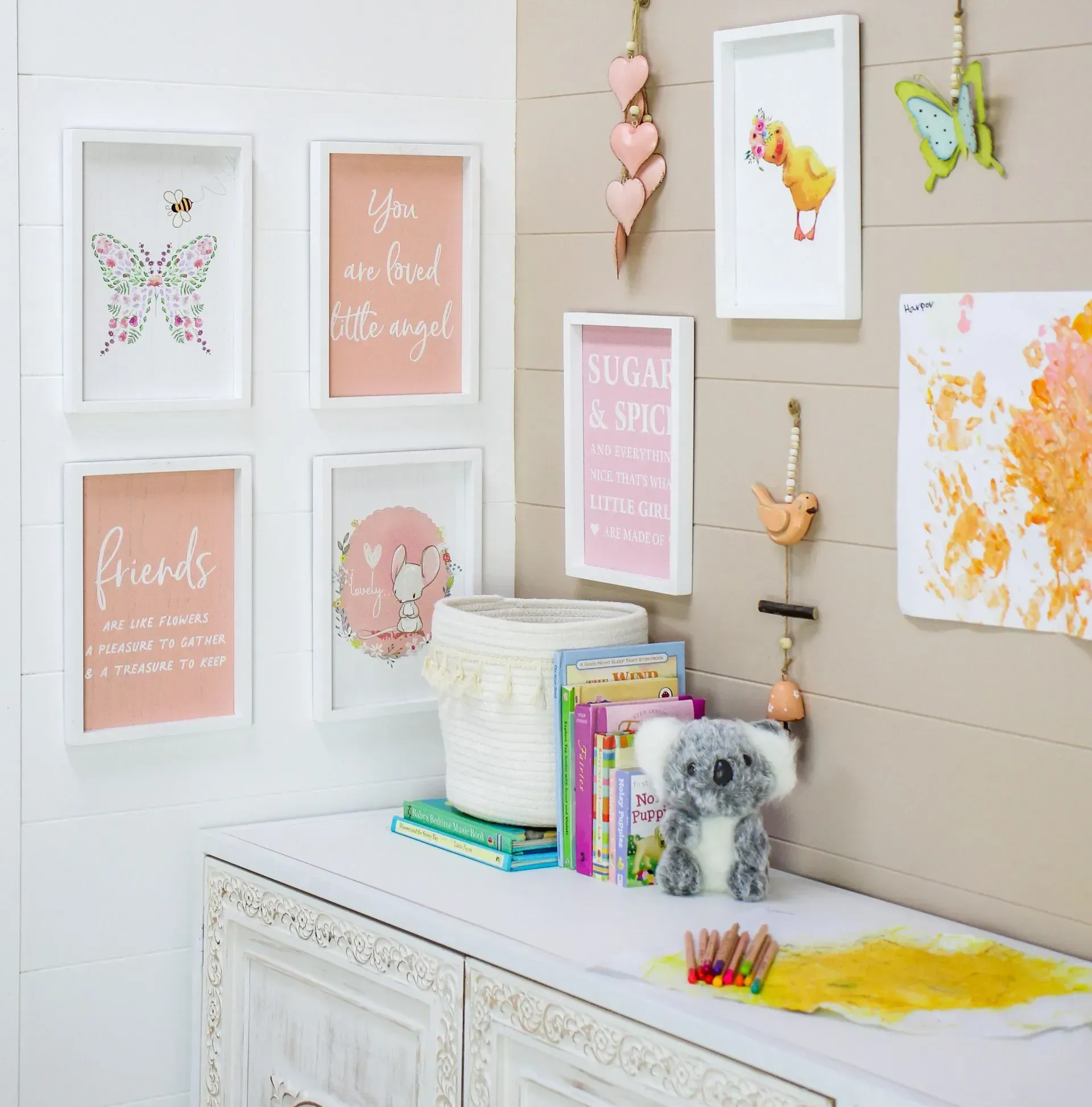 Pastel kids’ room with framed art, hanging decorations, and a decorated dresser with books and a plush toy
