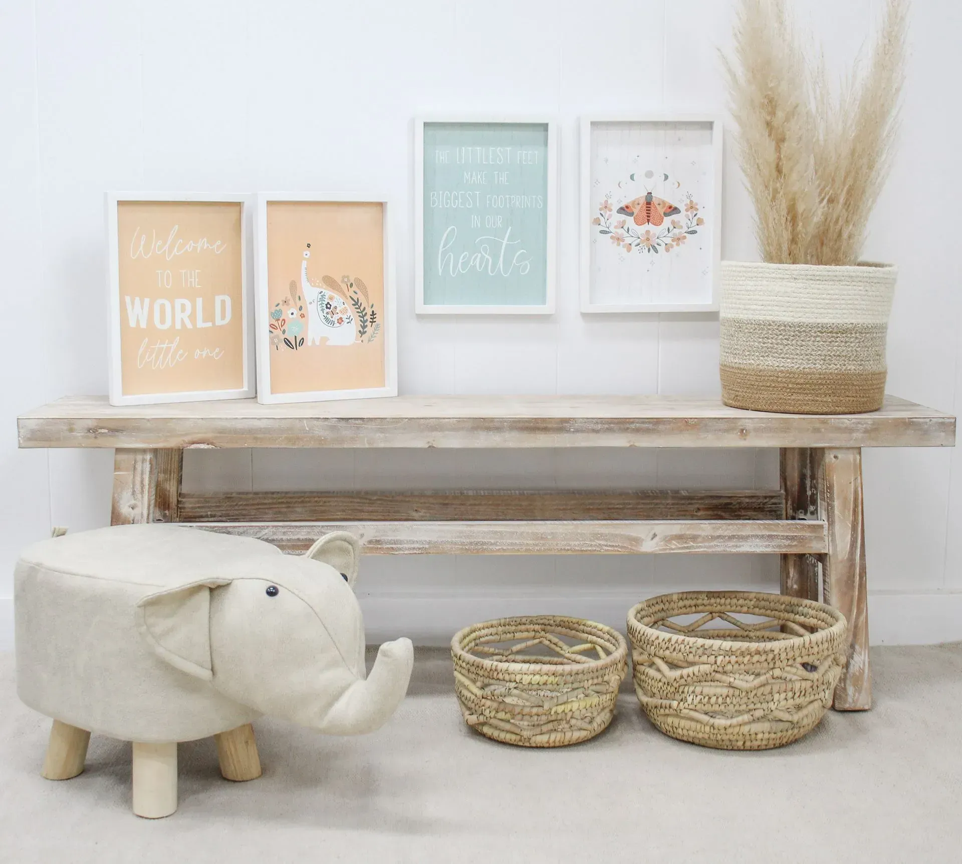 Neutral nursery decor with framed art, woven baskets, a bench, and a plush elephant stool on a light background