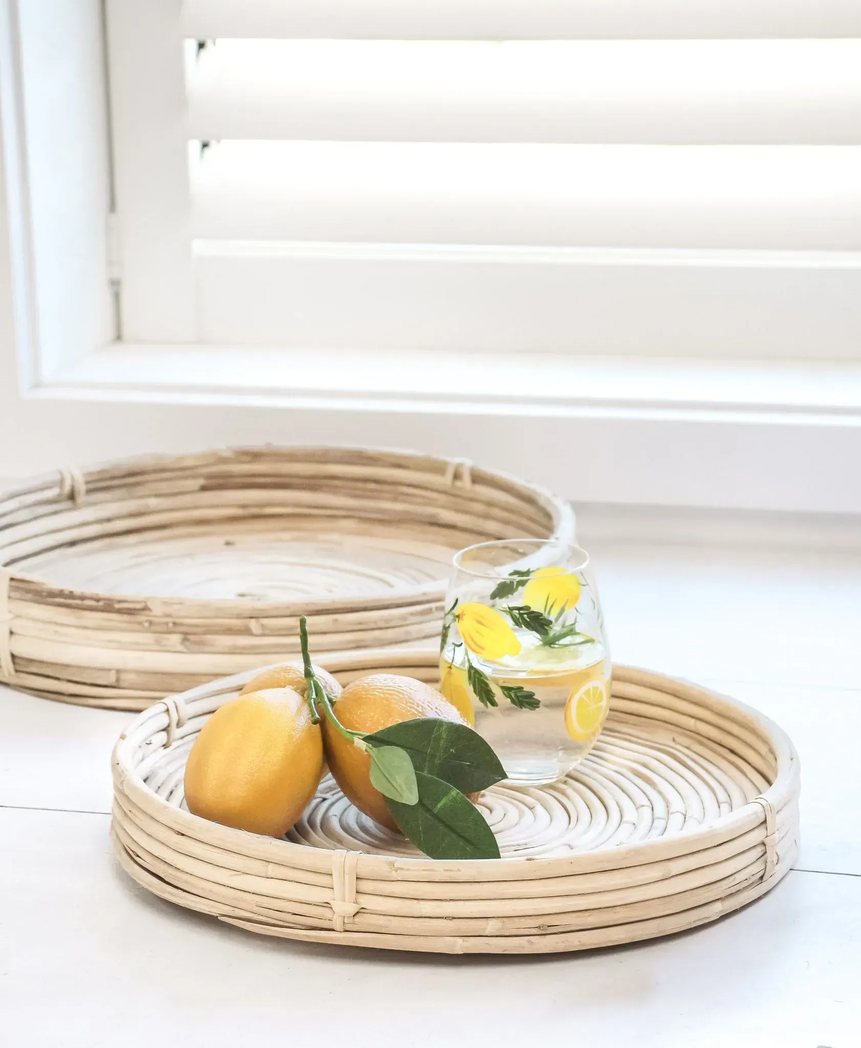 Woven trays with lemons and flowers on a white table by a window