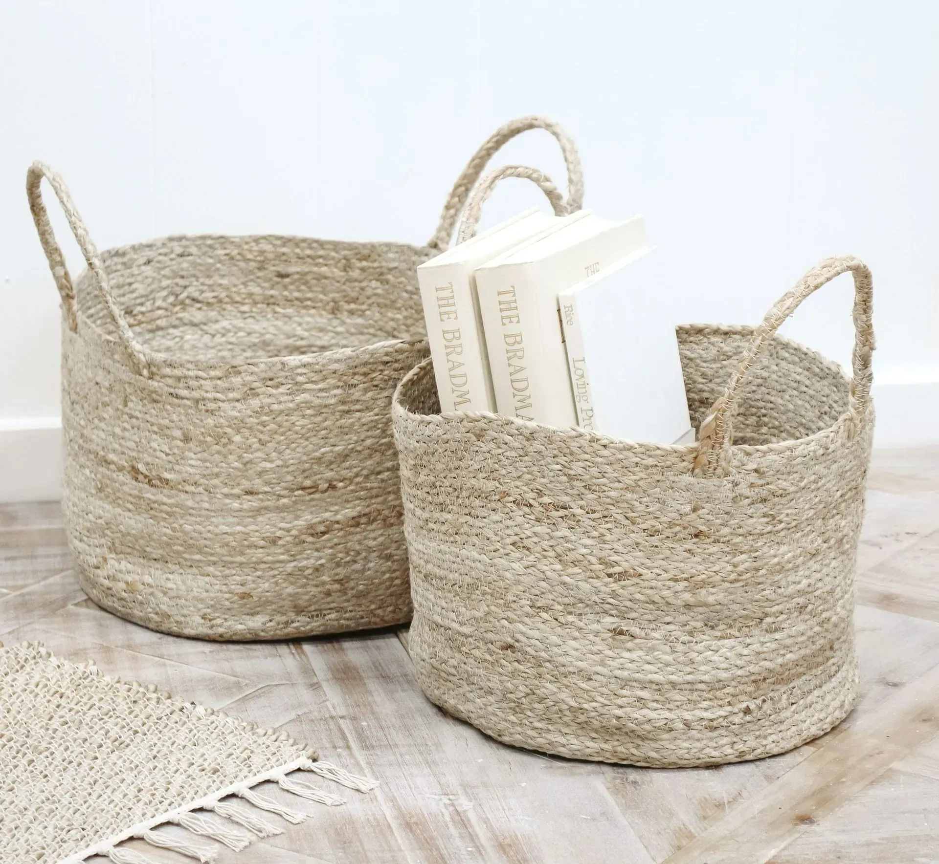 Two woven storage baskets with handles, one holding books, on a light wood floor