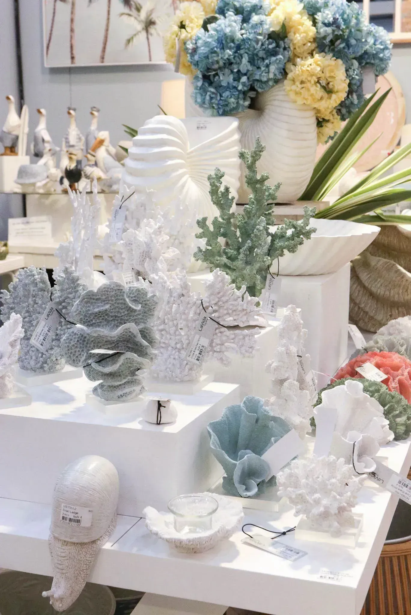 White tabletop display of pastel blue and white shell, coral, and floral decor with a vase of hydrangeas