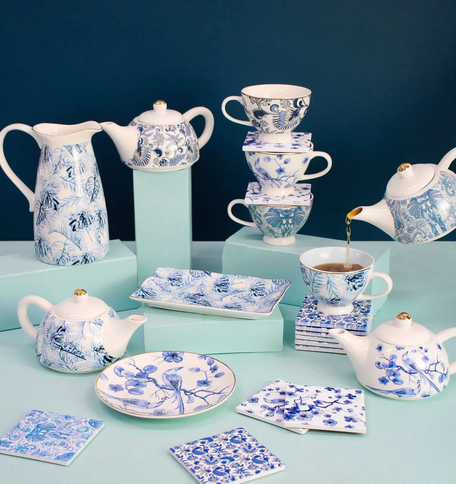 Blue-and-white porcelain tea set with teapots, cups, plates, and serving dishes on mint pedestals