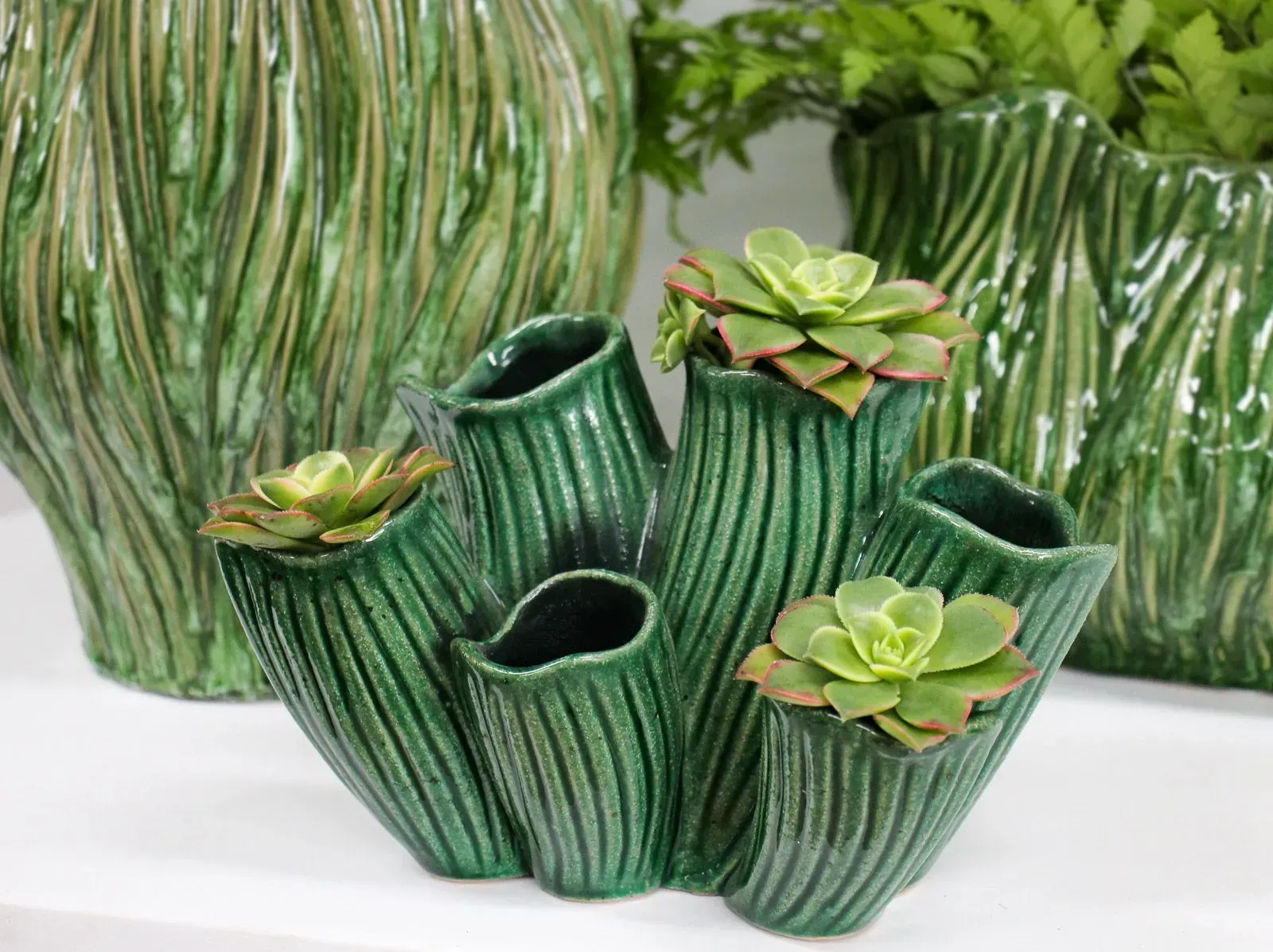 Green ceramic succulent planter with multiple hollow pots and small succulents, on a white background