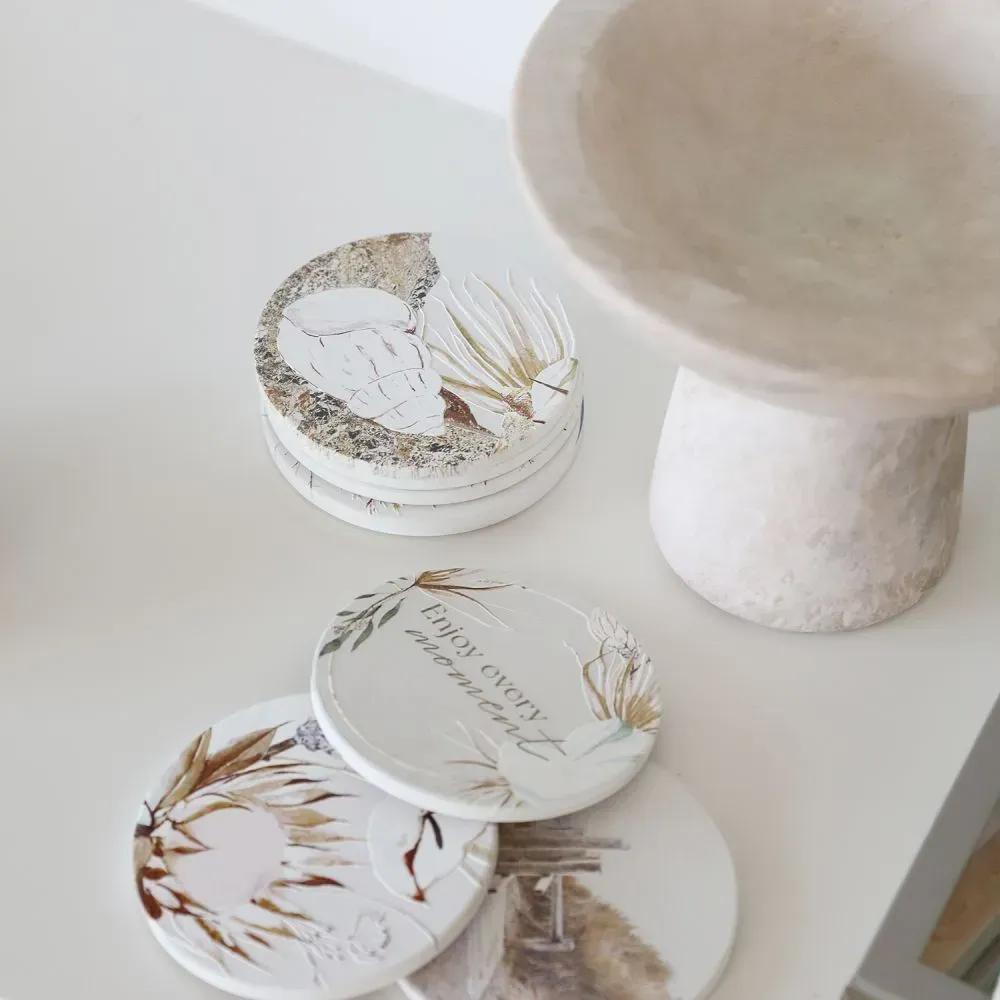 Stacked white round decor boxes with gold botanical designs on a white surface beside a beige pedestal table
