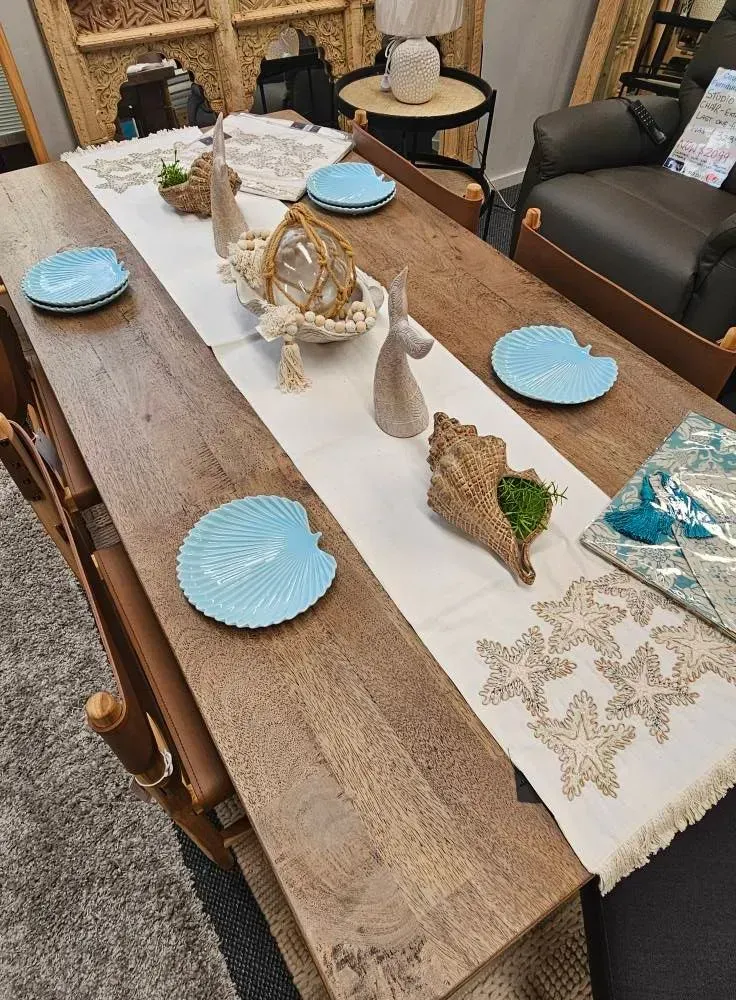 Dining table set with blue plates, white decor, and a beige floral runner in a living room