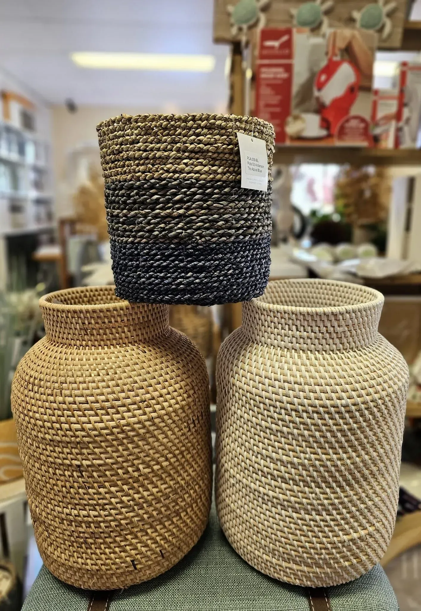 Three woven storage baskets stacked in a shop, in tan, cream, and dark navy colors.