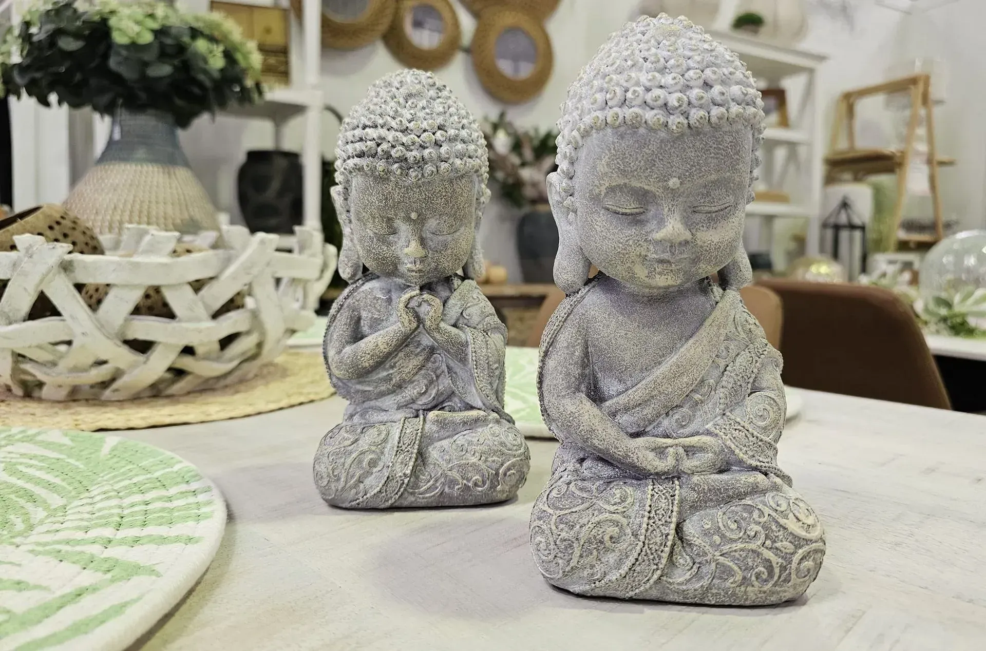Two textured gray Buddha statues seated on a table in a softly decorated room