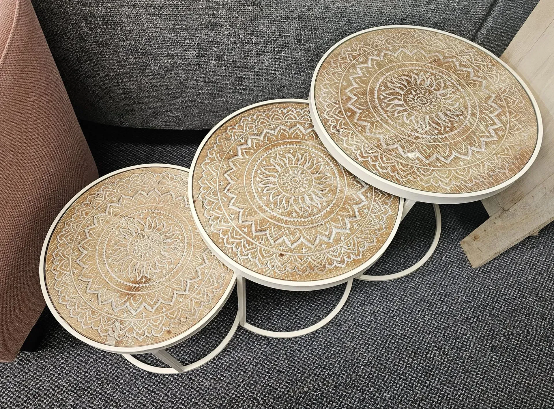 Three small round woven side tables with beige tops and white bases on a gray carpet beside a sofa
