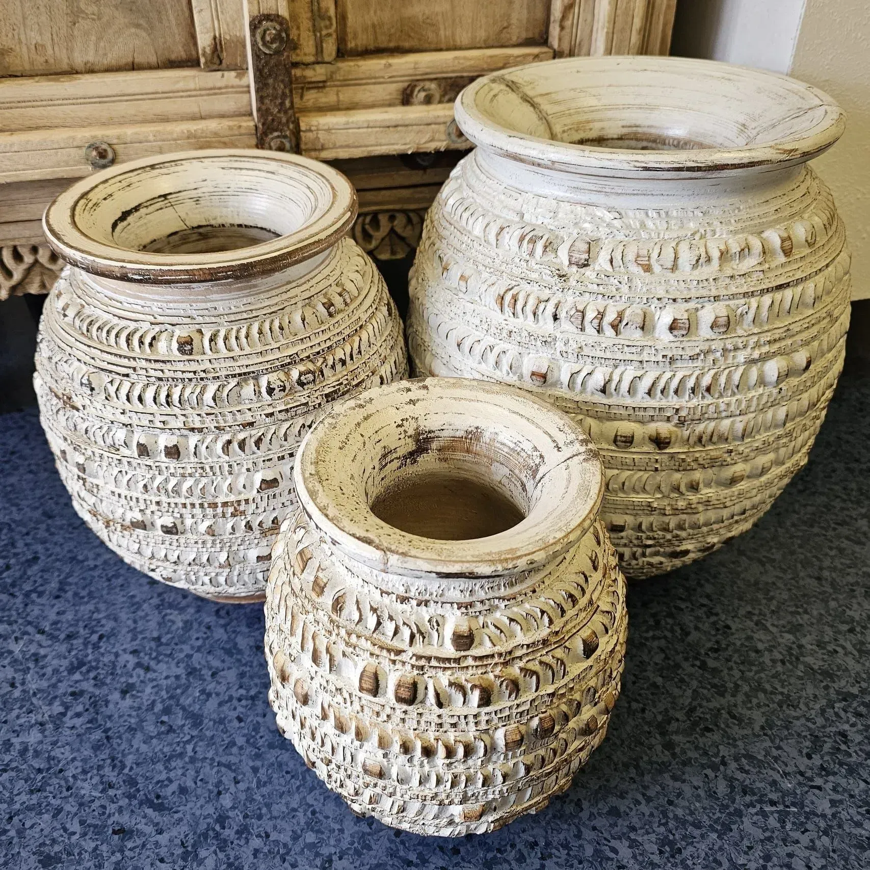 Three cream-colored woven ceramic vases on a blue carpet, with a wooden cabinet behind them