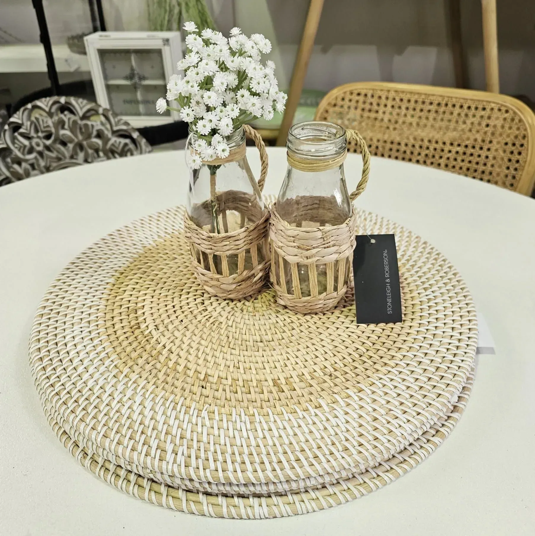 Round woven placemat with glass jars and a small white flower bouquet on a white table