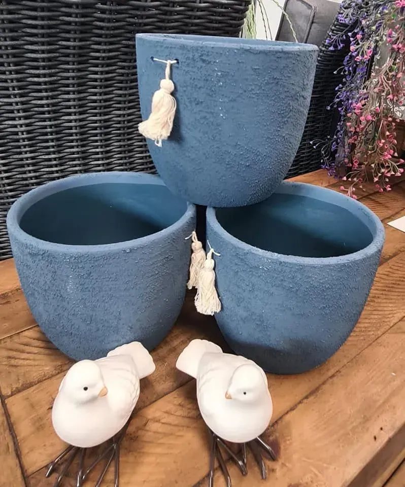 Three blue textured plant pots on a wooden deck with two white bird figurines in front.