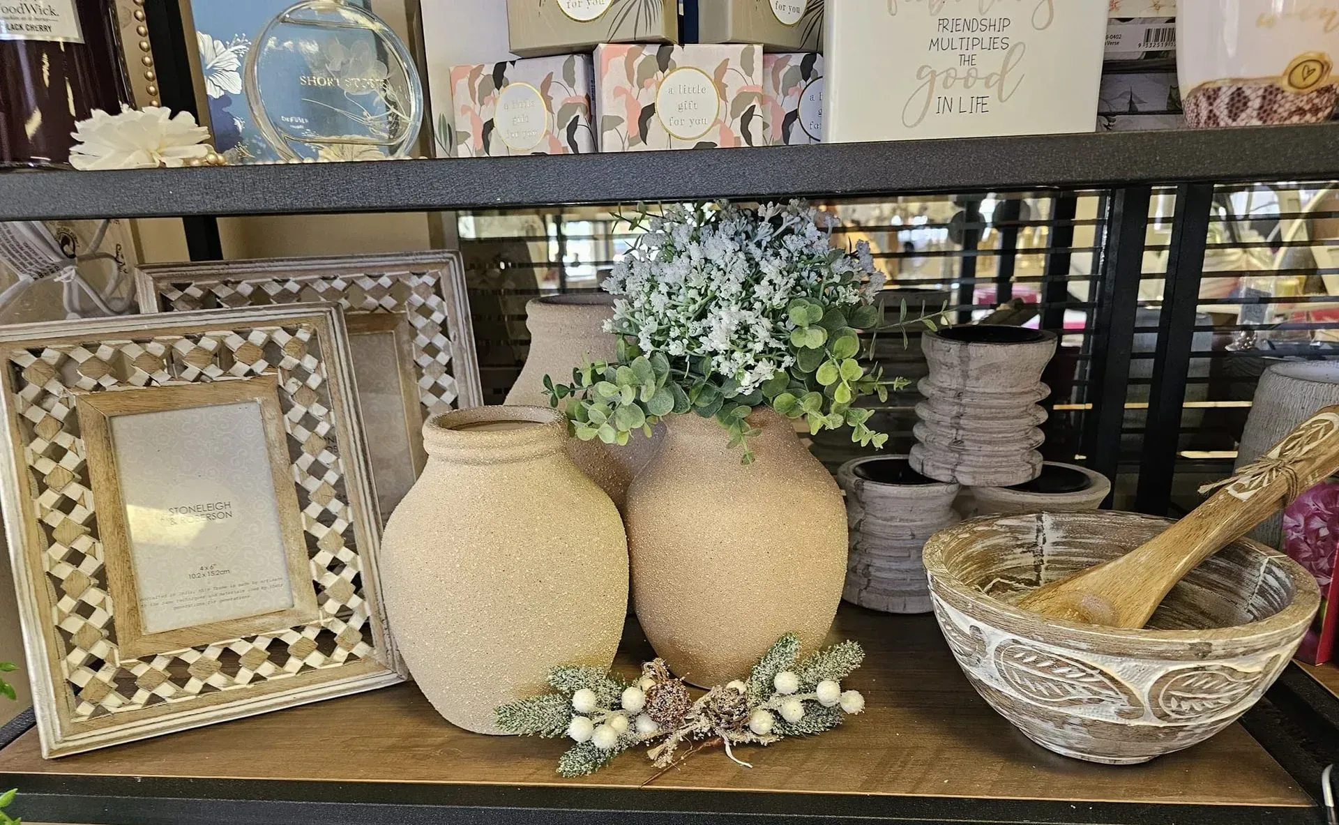 Decorative home display with beige vases, floral accents, a framed mirror, and a mortar and pestle on a shelf