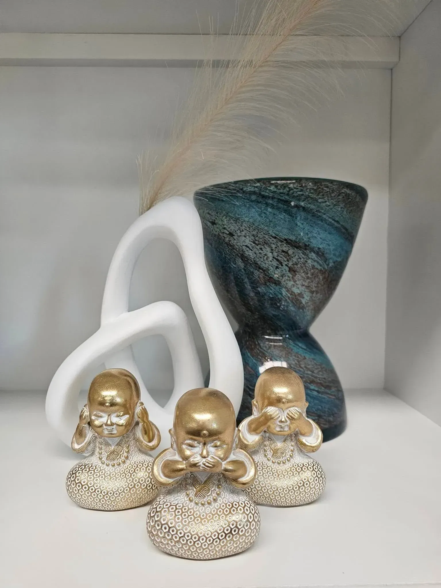 Three gold figurines in front of a white and blue decorative vase on a shelf
