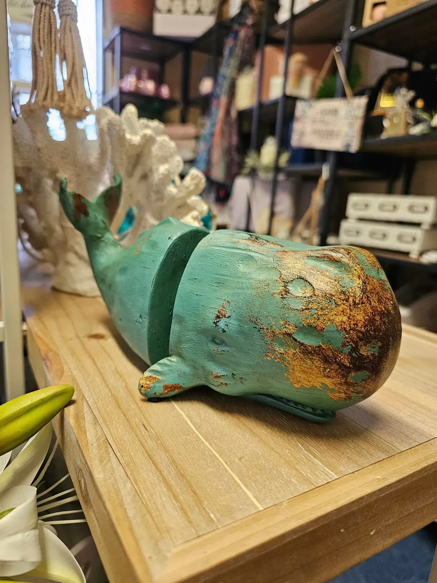 Small turquoise whale figurine with a rust-speckled finish on a wooden shelf in a shop
