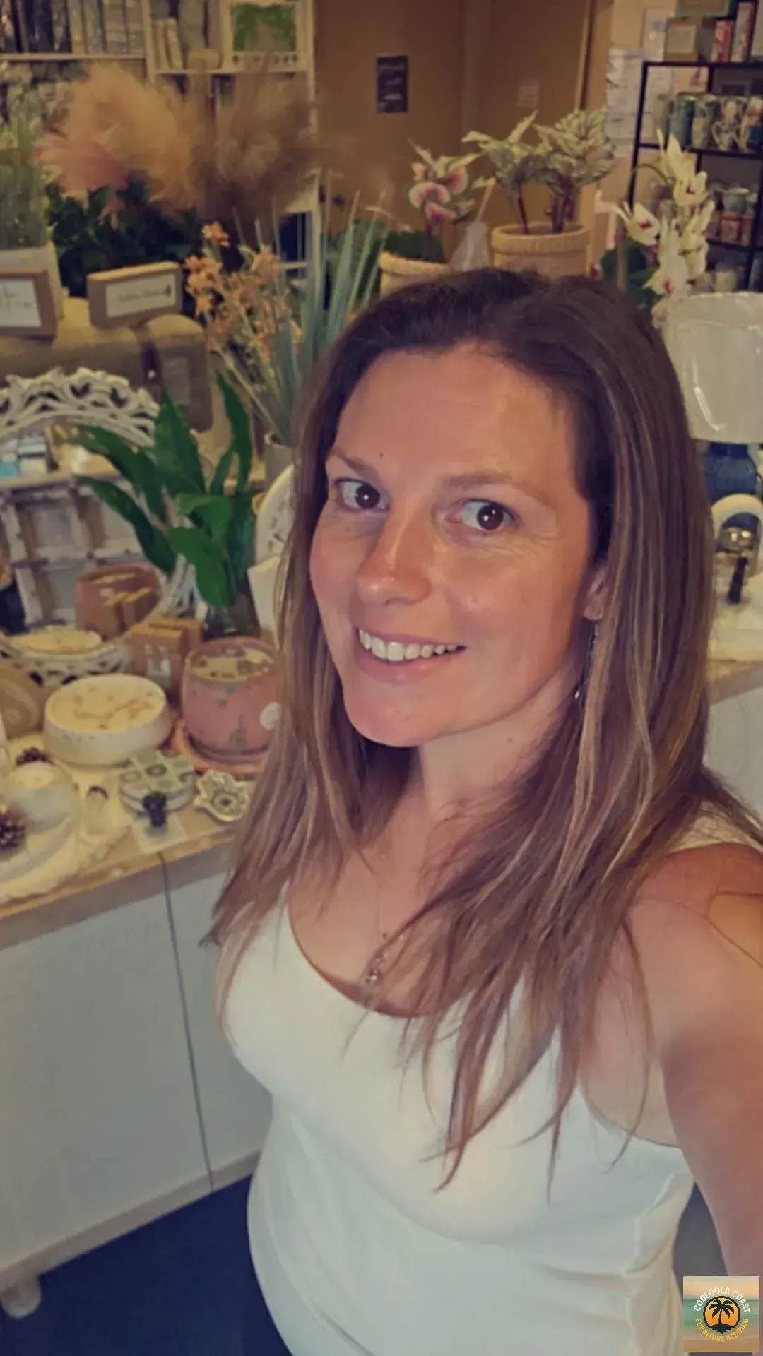 Smiling woman in a white top posing in a flower shop with plants and decor.