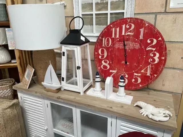 Decorative shelf with white lanterns, sailboat decor, and a large red wall clock above a white cabinet