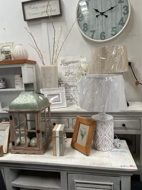 Decorative tabletop display with a lamp, framed art, lantern, and large wall clock in a vintage-style room