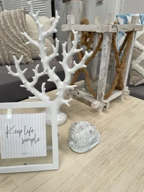 White coral decor and framed sign on a light wood shelf with a small shell ornament