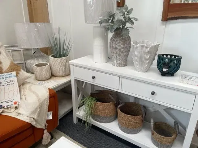Decorative white console table with vases and plants beside an orange chair in a bright room