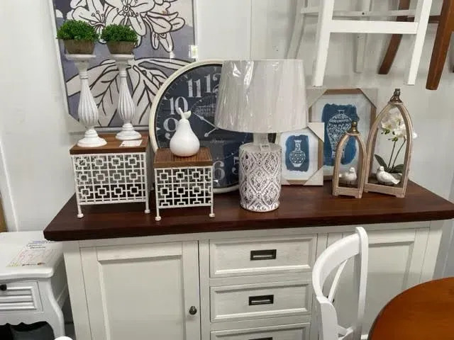 Decorative white and blue tabletop display with lamps, clocks, and framed art on a cabinet