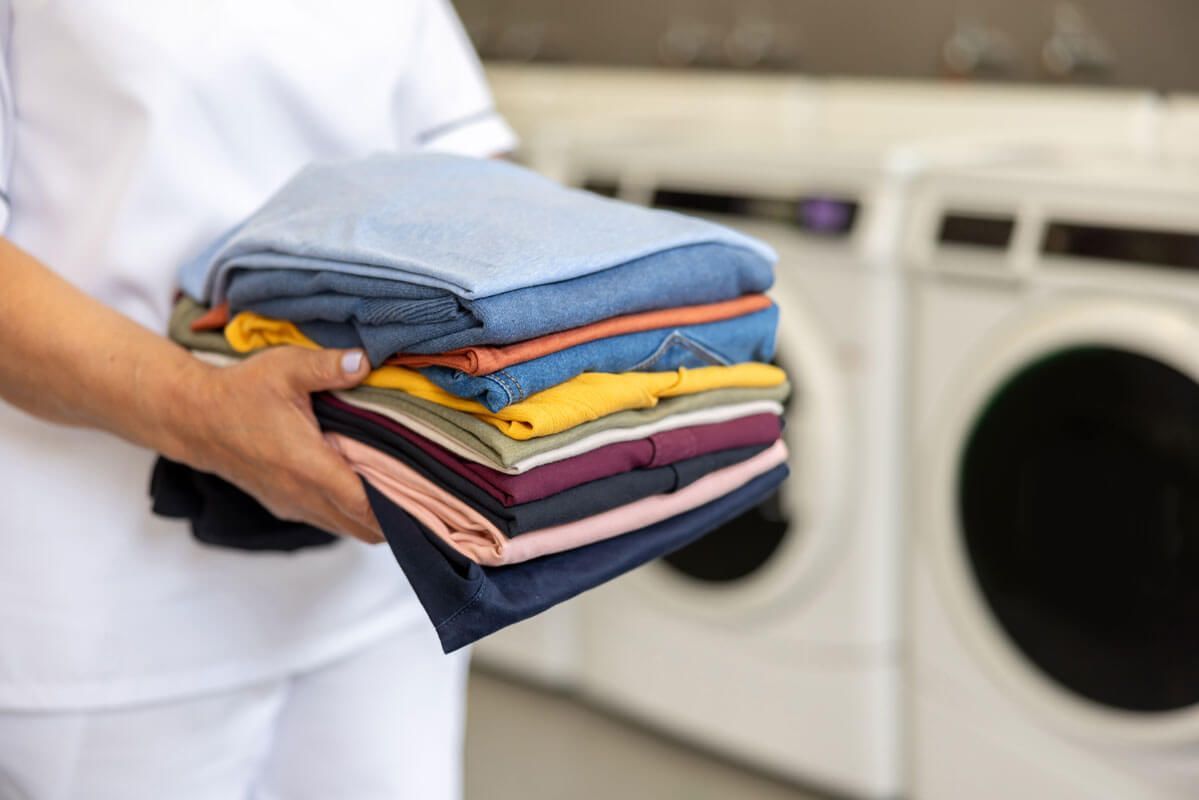 Person holding a stack of folded colorful laundry near a washing machine