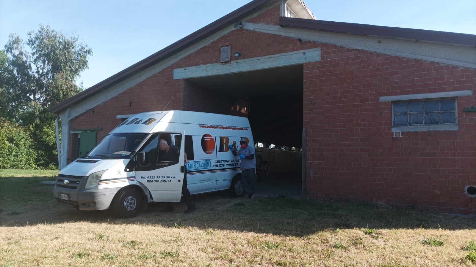 Un furgone bianco parcheggiato davanti a un edificio in mattoni rossi con un grande portone da garage aperto.