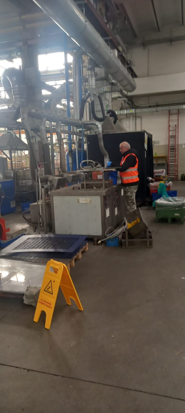 Operaio con giubbotto di sicurezza arancione ispeziona le attrezzature in un'officina industriale.