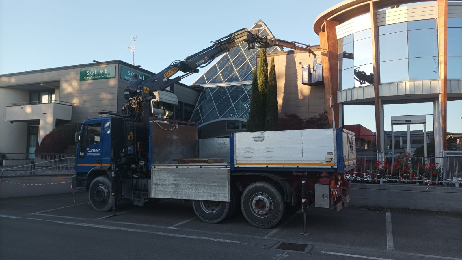 Camion che trasporta detriti davanti a un edificio danneggiato e a un cantiere.