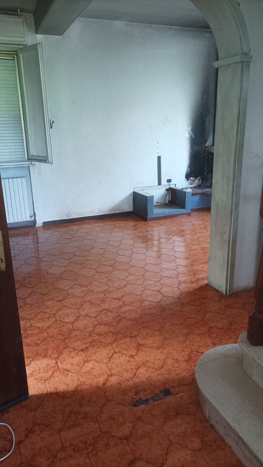 Stanza vuota con pavimento piastrellato con motivi arancioni, pareti bianche e un piccolo lavandino o zona di servizio sul retro.