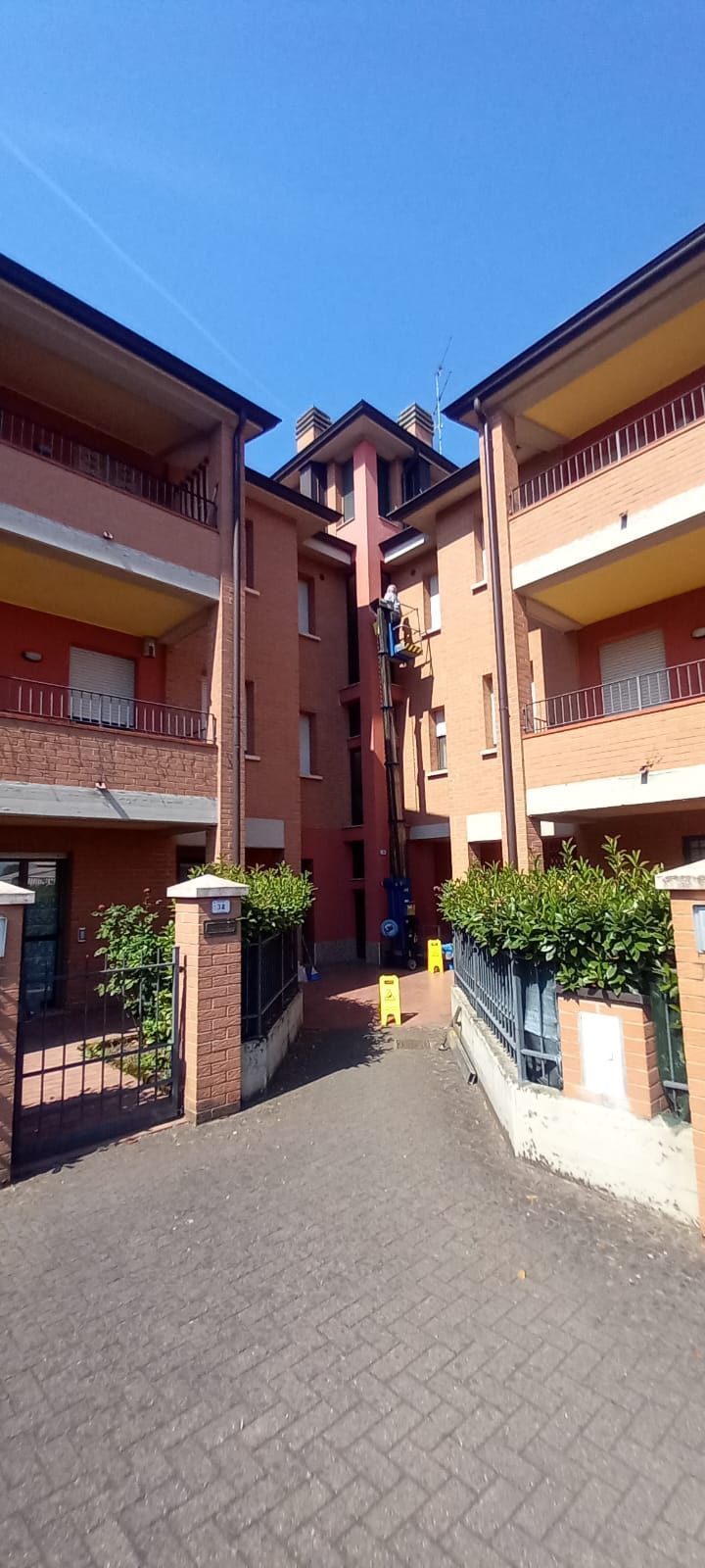 Stretto passaggio pedonale tra palazzi arancioni sotto un cielo azzurro brillante, con arbusti in vaso all'ingresso.