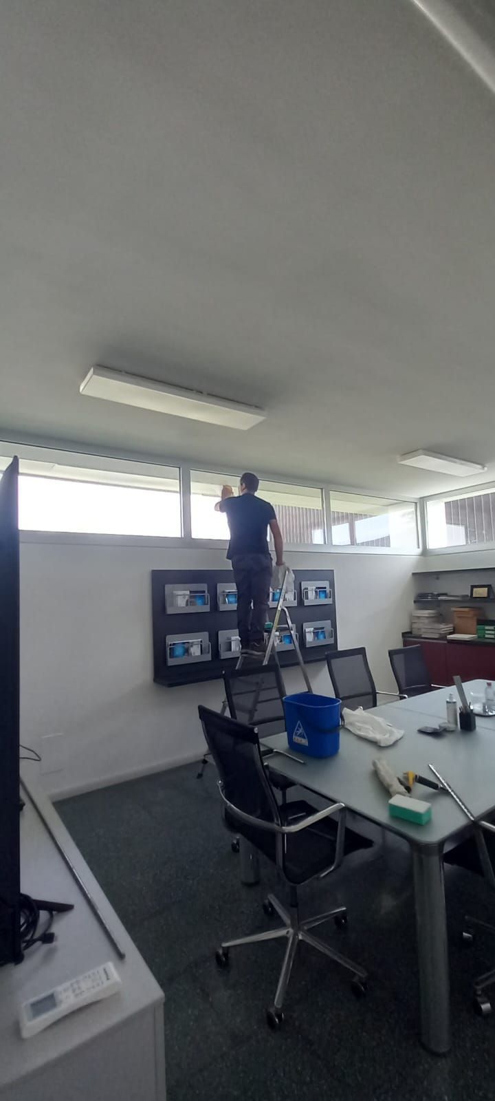Una persona in piedi su un armadietto in un ufficio luminoso, si protende verso le luci del soffitto.