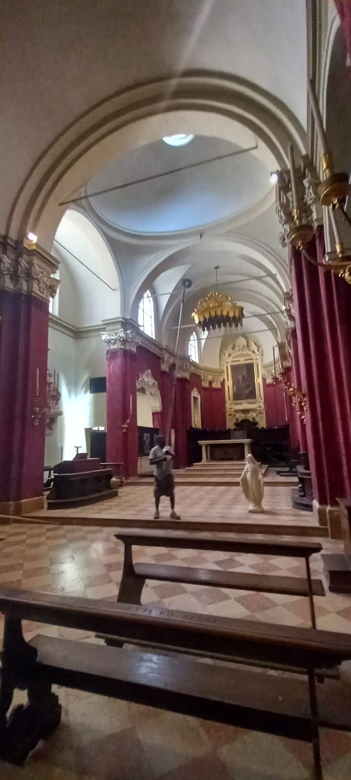 Interno maestoso della chiesa con drappi rossi, soffitti a volta, panche e alcune persone vicino all'altare.