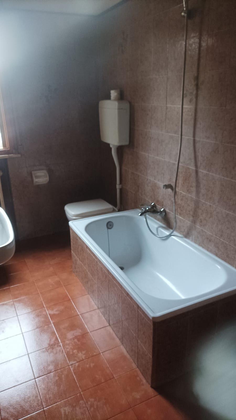Piccolo bagno con piastrelle in terracotta, vasca da bagno, WC e scaldabagno a parete.