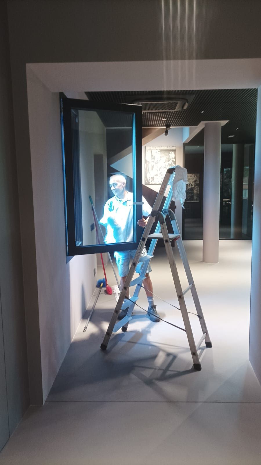 Due operai sulla soglia di una porta, uno su una scala, in un luminoso corridoio interno.