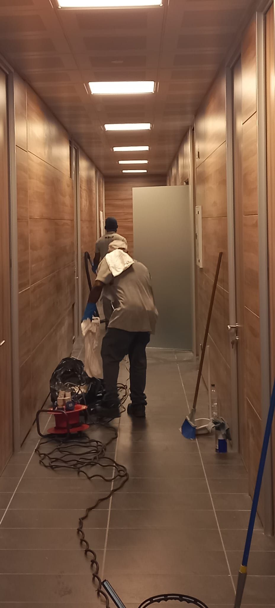 Una persona sta lavorando al cablaggio in uno stretto corridoio con lampade a soffitto a vista e attrezzi sul pavimento.